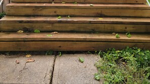 Un ensemble de marches en bois menant à une porte de couleur sombre, surmontée d’une petite fenêtre.