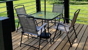 Une terrasse avec une table et des chaises, un parasol et une vue sur un espace verdoyant avec des arbres.