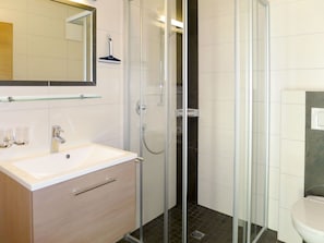 A modern bathroom with a glass-enclosed shower, a white sink with a chrome faucet, and a toilet.