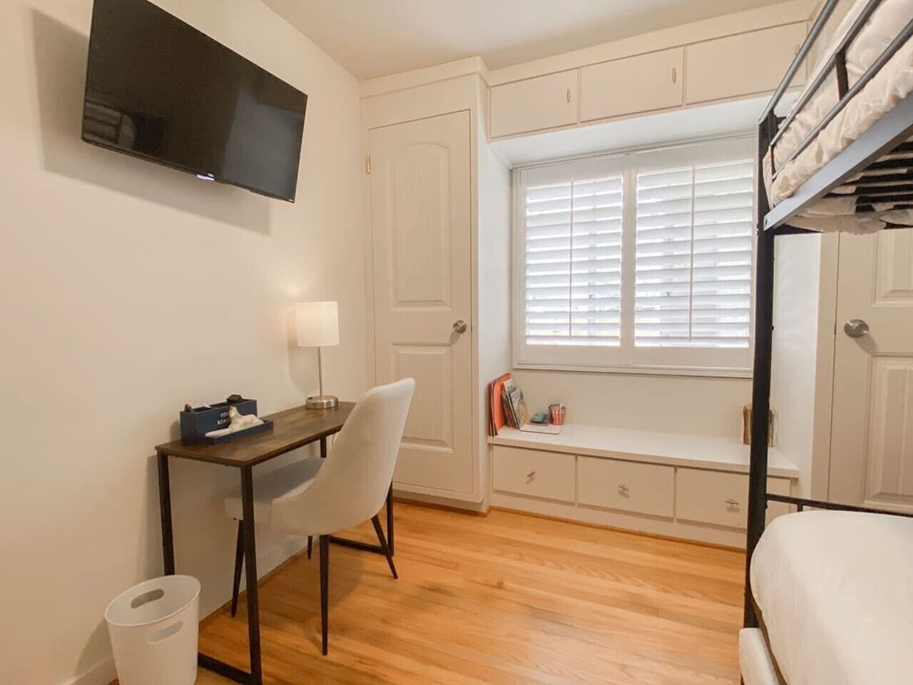 Een kleine kamer met een bureau, stoel en raam met zonwering.
