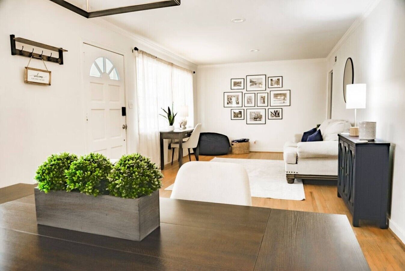 Ein modernes Wohnzimmer mit einer Couch, einem Couchtisch, einem Esstisch mit Stühlen, einer Pflanze und gerahmten Bildern an der Wand.