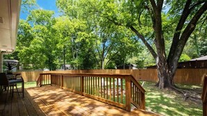A wooden deck with a railing, surrounded by trees and a wooden fence.