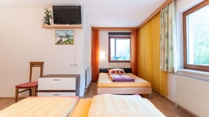 A hotel room with two beds, a TV on a shelf, a desk, a chair, and a window with curtains.