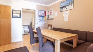 A dining area with a wooden table and grey upholstered chairs, a brown sofa, and a carpeted floor.