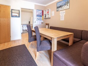 A dining area with a wooden table and grey upholstered chairs, a brown sofa, and a carpeted floor.