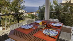 A dining table set with plates, glasses, and cutlery on a balcony overlooking the sea. - Beautiful apartment for 4 guests with pool, WIFI, A/C, TV and terrace (Santa Isabel)