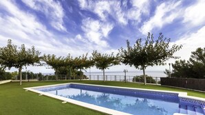 A rectangular swimming pool with a decorative edge, surrounded by well-maintained artificial grass, trees, and a view of the sea. - Beautiful apartment for 4 guests with pool, WIFI, A/C, TV and terrace (Santa Isabel)