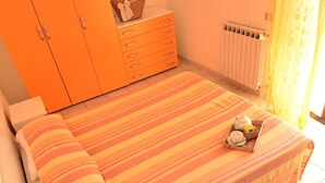 A bedroom with a striped bedspread, a dresser with drawers, a radiator, and a basket with breakfast items on the bed. - Nice apartment for 4 guests with WIFI, TV, balcony and pets allowed (Silvi)