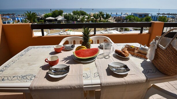 A table set with a watermelon, pineapple, croissants, and a teapot on a balcony overlooking the sea. - Nice apartment for 4 guests with WIFI, TV, balcony and pets allowed (Silvi)
