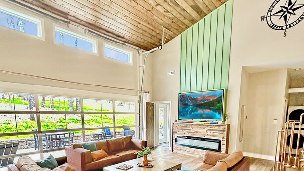 Un salón amplio con un televisor grande, muebles de madera y vistas al exterior.