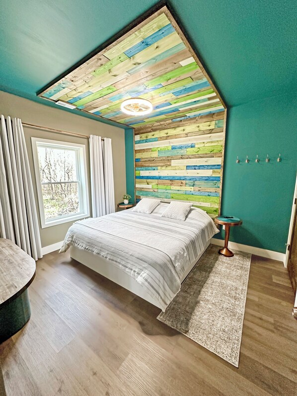 A bedroom with a sloped ceiling, a bed with a white bedspread, a round table, and a small side table.