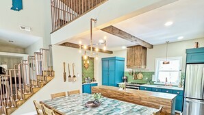 Una cocina amplia con una isla central, una escalera de madera y un comedor con una mesa grande.