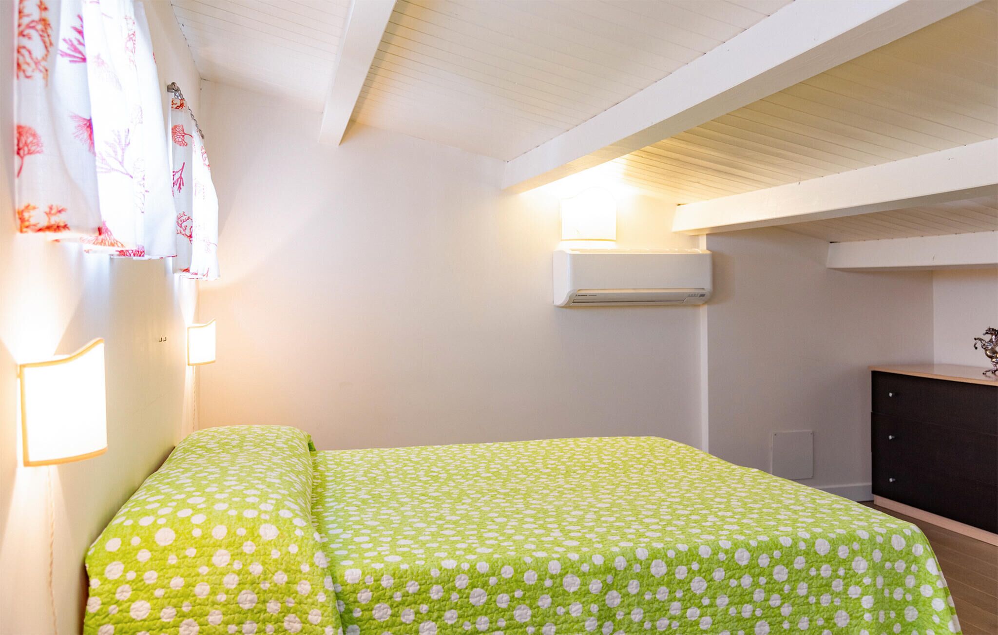 A bedroom with a bed, a wall-mounted air conditioner, and a desk with a chair.