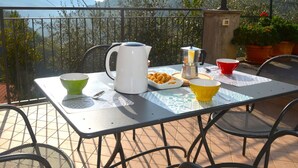 Eine Terrasse mit Esstisch, gedeckt mit Kaffeekanne, Schüsseln und einer Teller voller Essen.