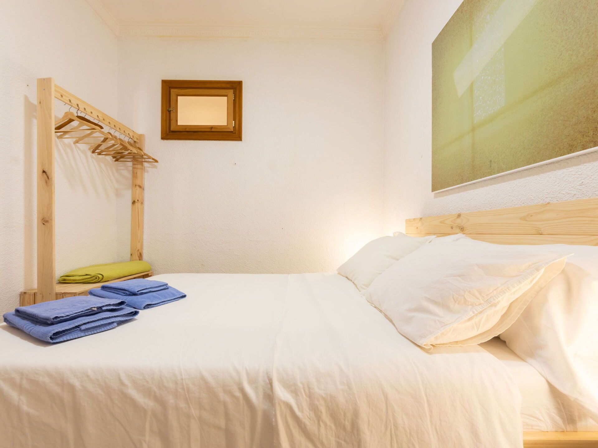 Un dormitorio con cama, un tendedero de madera y un cuadro en la pared.