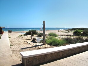Een strand met een houten looppad naar het water, een stenen muur en een volleybalnet.