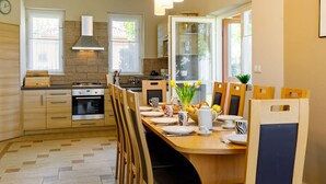 A modern kitchen with wooden cabinets, a gas stove, and a dining area with a table set for four. - Stunning private villa for 12 people with WIFI, A/C, TV, patio and pets allowed (Balatonboglár)