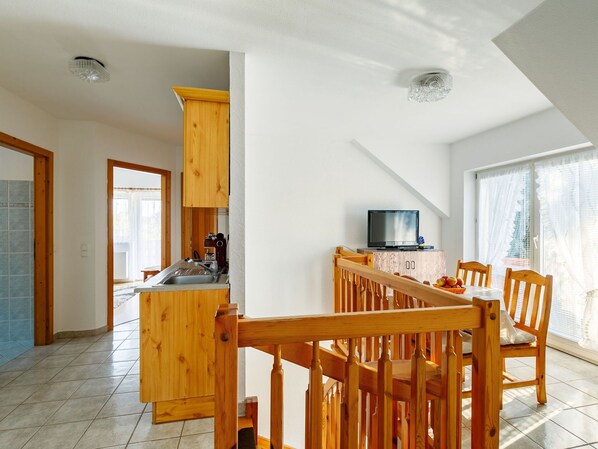 Een moderne keuken met houten kasten, een eethoek met een houten tafel en stoelen, en een televisie op een kast.