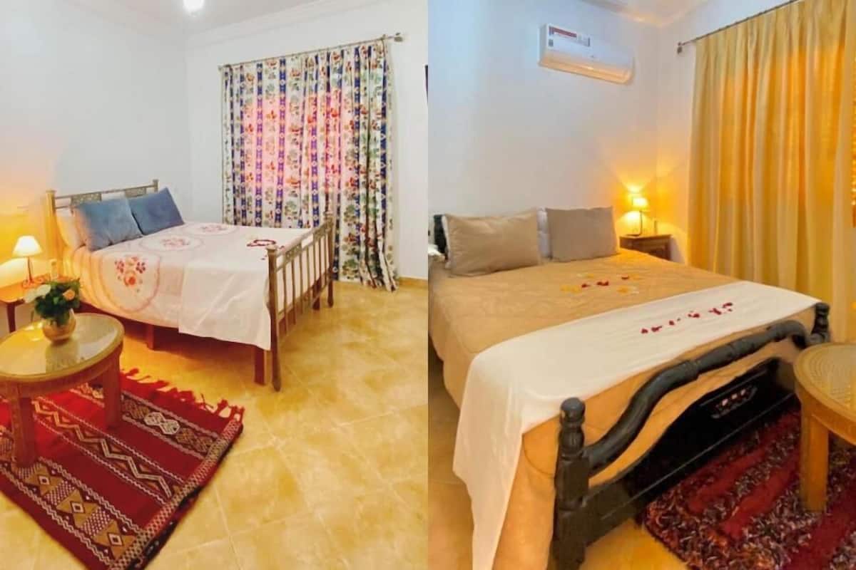 Une chambre à coucher comprenant un lit, une table de chevet, une lampe, une fenêtre avec des rideaux et un luminaire au plafond.