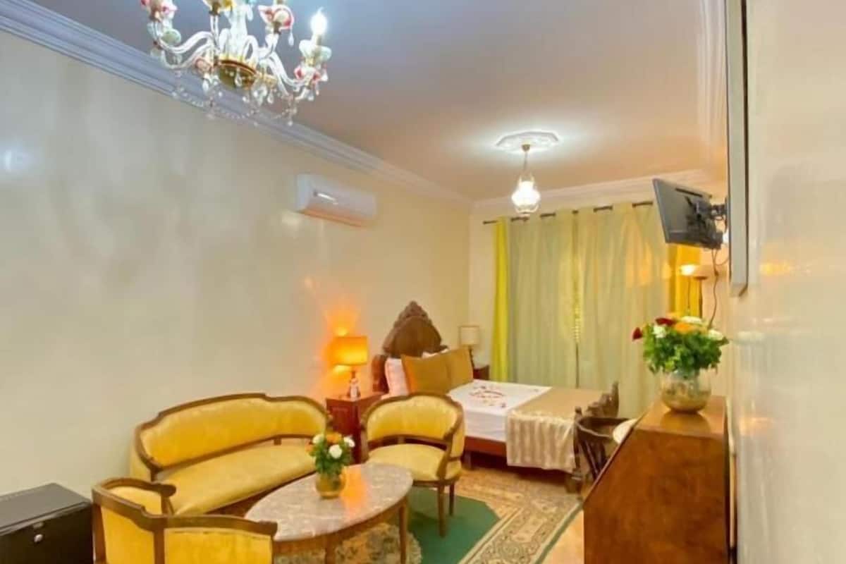 Un salon comprenant un ensemble de canapés, une table basse, un lustre et un téléviseur fixé au mur.