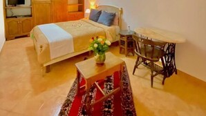 Um quarto aconchegante com cama, mesa de cabeceira e uma pequena mesa com um vaso de flores.