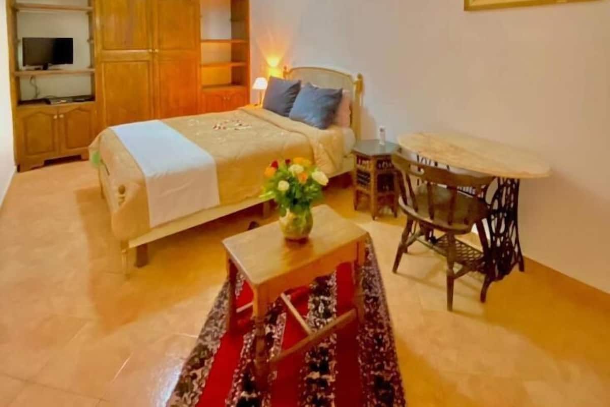 Une chambre confortable avec un lit, une table de chevet et une petite table sur laquelle est posé un vase de fleurs.