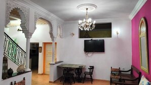 Uma sala de estar com área de jantar, lustre, televisão e decoração tradicional.