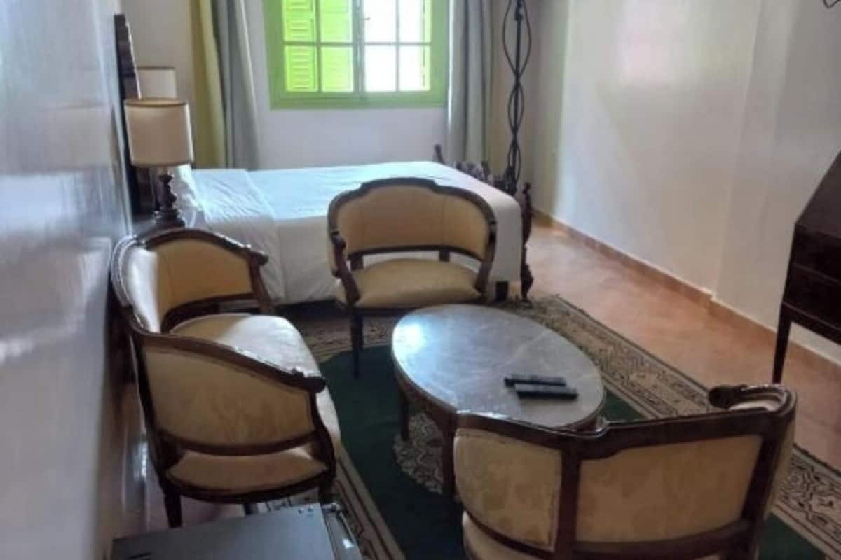 Une chambre d’hôtel comprenant un lit, deux fauteuils, une petite table ronde, une lampe et un téléviseur.