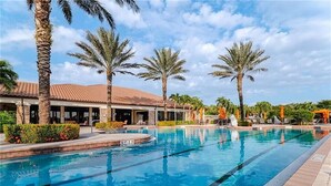 A swimming pool with clear blue water, surrounded by palm trees and a building with a tiled roof. - Welcome to this Endearing Naples Home! (Naples)