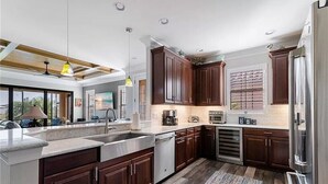 A modern kitchen with dark wooden cabinets, stainless steel appliances, and a large island with a sink. - Welcome to this Endearing Naples Home! (Naples)