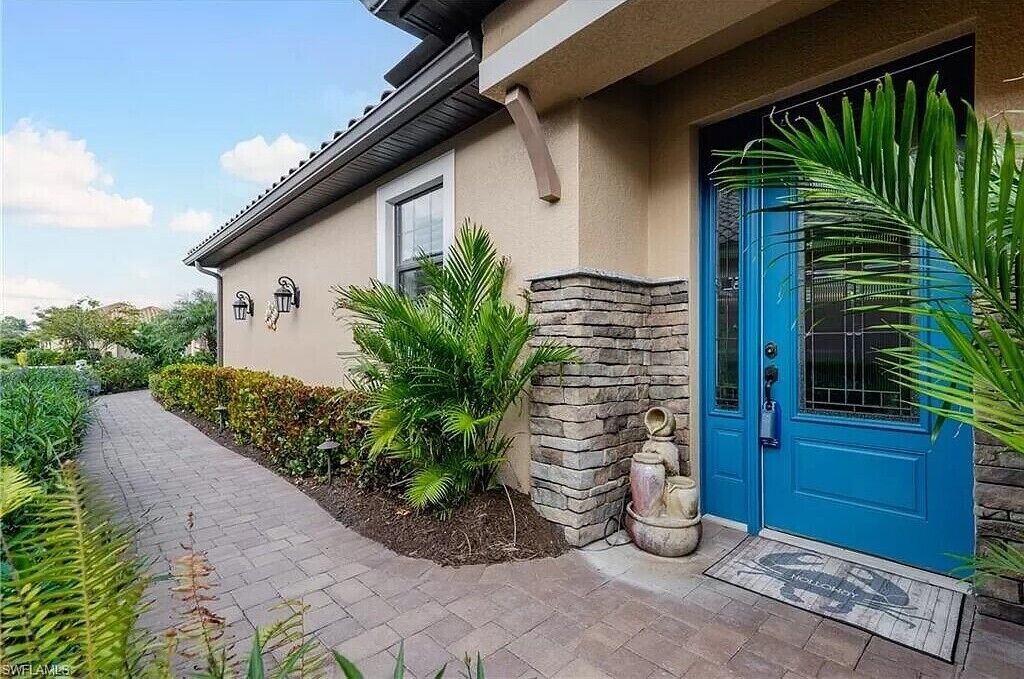 A house with a blue door, a stone wall, and a pathway leading to the entrance.