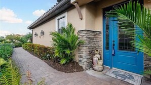 A house with a blue door, a stone wall, and a pathway leading to the entrance. - Welcome to this Endearing Naples Home! (Naples)