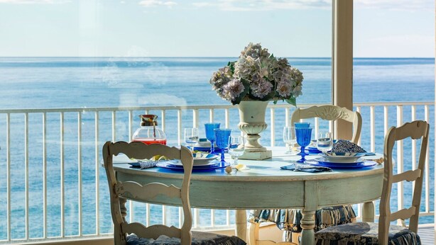 A table set for two with a view of the sea, a vase of flowers, and a bottle of red wine. - Lovely apartment for 4 guests with WIFI, TV and balcony (Riva Ligure)