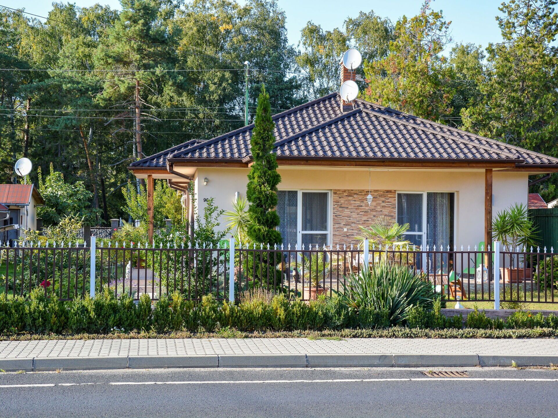 A two-story house with a tiled roof, satellite dishes, and a fenced yard.