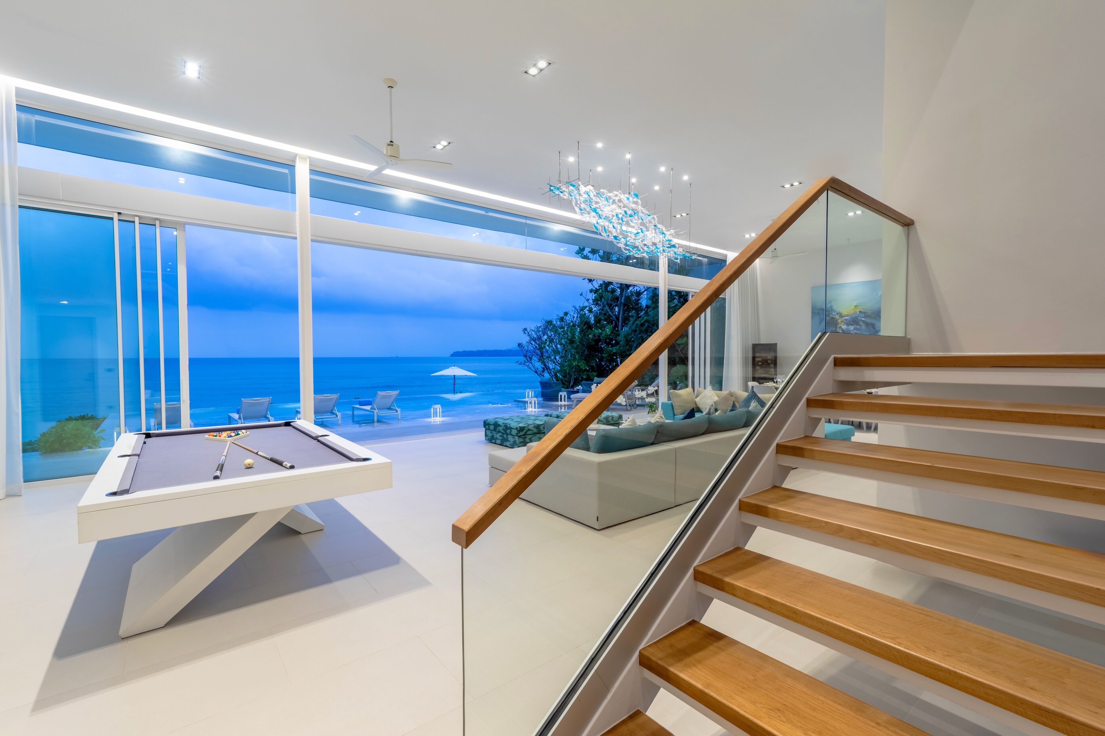Een modern interieur met een pooltafel, een trap en uitzicht op zee.