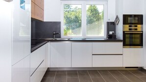 A modern kitchen with white cabinets, a black countertop, a Bosch oven, and a window with a view of trees. - Wonderful private villa for 8 guests with terrace and pets allowed (Keszthely)