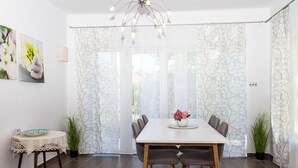 A dining area with a white table, four chairs, a chandelier, and patterned curtains. - Wonderful private villa for 8 guests with terrace and pets allowed (Keszthely)