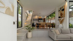Ein modernes Wohnzimmer mit einer Couch, einem Esstisch und Stühlen. Eine Treppe führt auf eine höhere Ebene.
