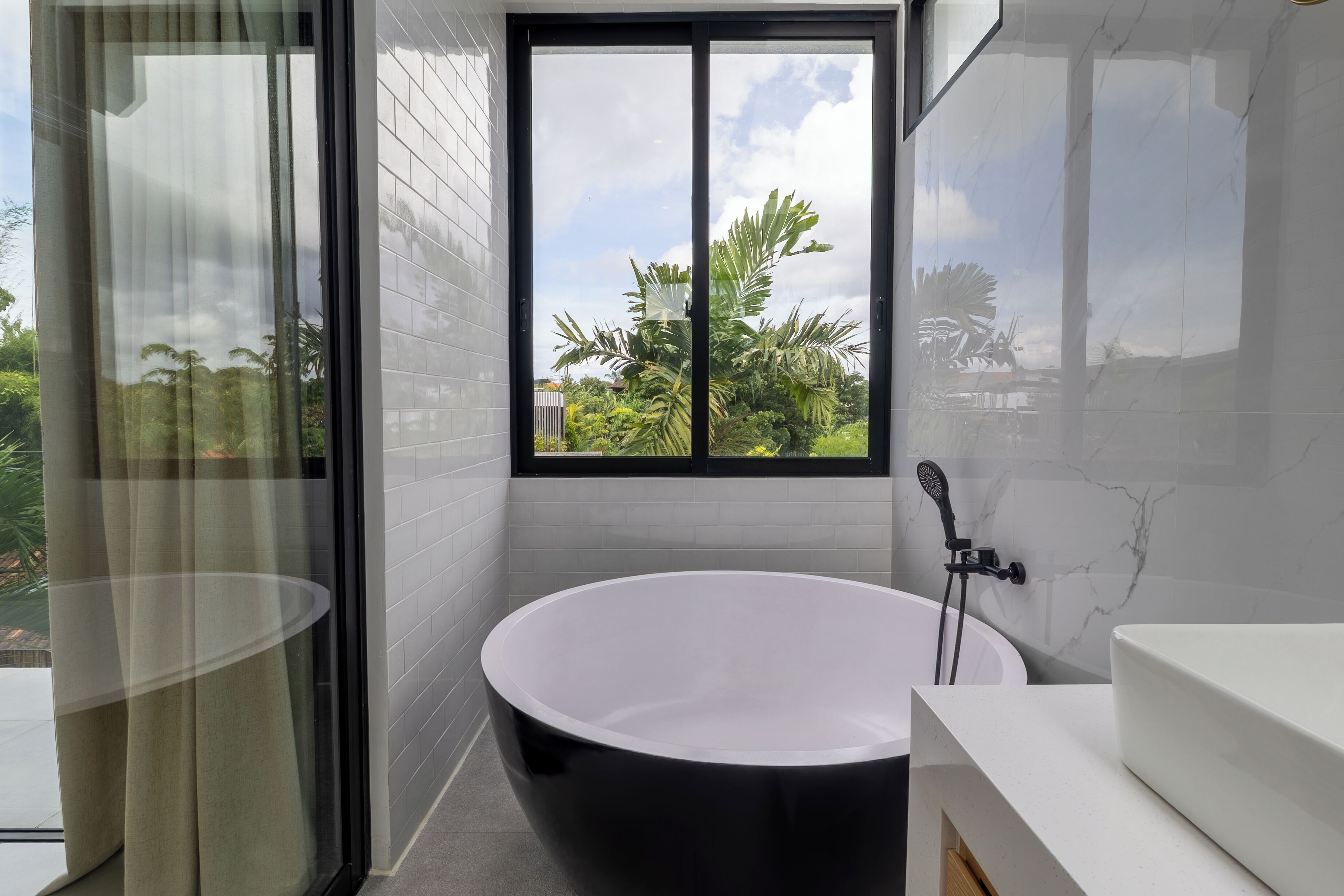 Un baño moderno con una bañera independiente, un ventanal grande y un tocador blanco.