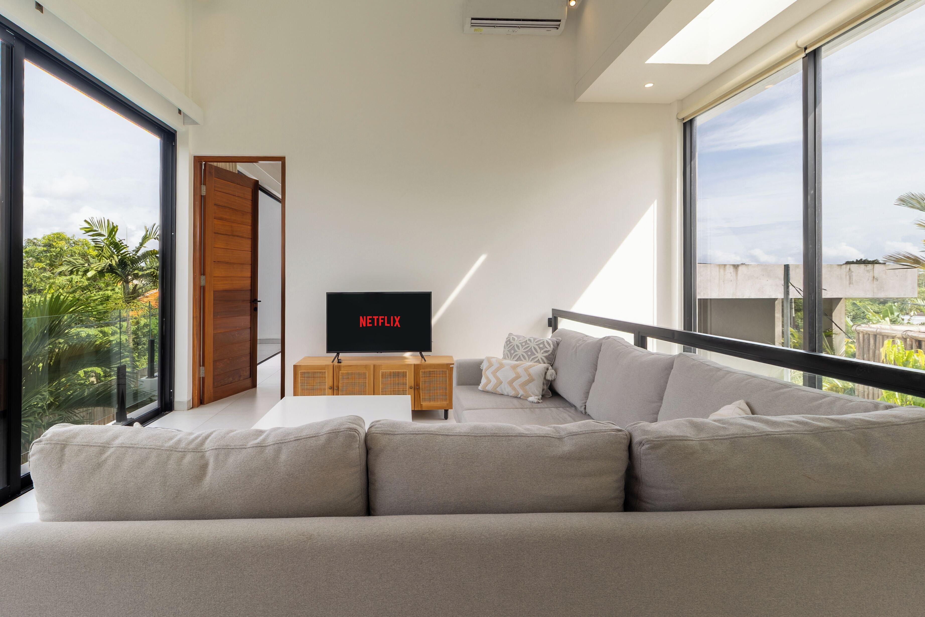 A modern living room with a large sofa, a wooden cabinet, and a flat-screen TV displaying 'NETFLIX'.