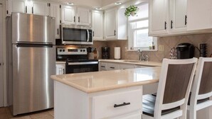 Una cocina moderna con armarios blancos, electrodomésticos de acero inoxidable, una isla central y una ventana con una planta.