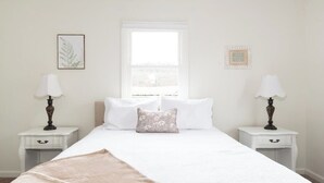 Un dormitorio con una cama grande, dos mesitas de noche con lámparas, una ventana y un cuadro en la pared.