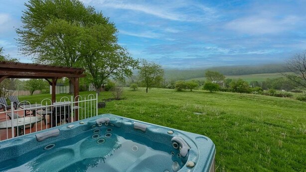 Un jacuzzi en un jardín con césped, una pérgola y vistas al campo.