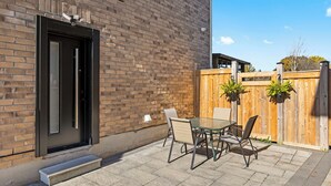 Eine Terrasse mit Glastisch und Stühlen, ein Holzzaun und ein Backsteinhaus.