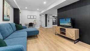 Ein modernes Wohnzimmer mit einem blauen Sofa, Holzböden, einem Fernseher auf einem Holztisch und einer Wand mit vertikalen Linien.