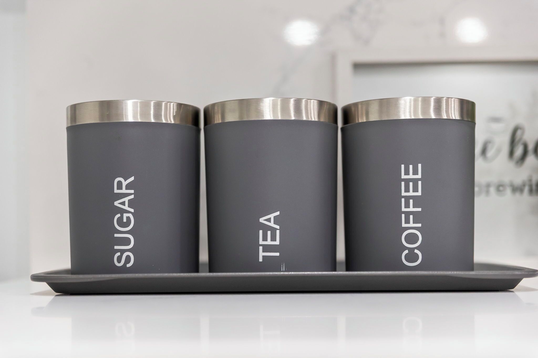 Three cylindrical containers labeled 'SUGAR,' 'TEA,' and 'COFFEE' on a tray.