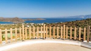 A coastal view from a balcony with a wooden fence, overlooking a beach and distant mountains. - Joy of the Sea Villa (Agios Nikolaos)