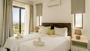 A hotel room with two beds, a large window with curtains, an air conditioning unit, and bedside lamps. - Joy of the Sea Villa (Agios Nikolaos)