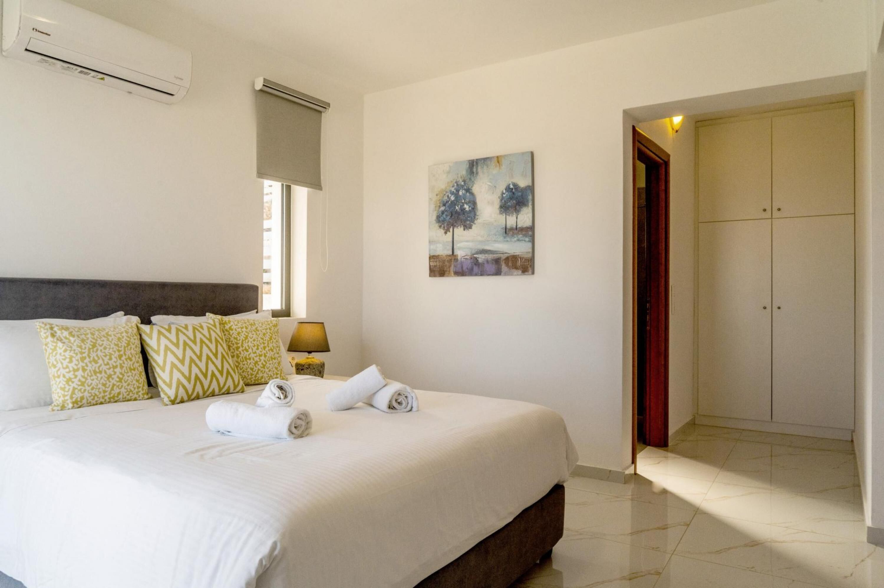 A hotel room with a large bed, a painting on the wall, an air conditioning unit, and a wardrobe.