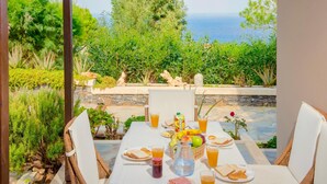 Mesa posta para o café da manhã, com vista para o mar, rodeada por vegetação exuberante e paredes de pedra.